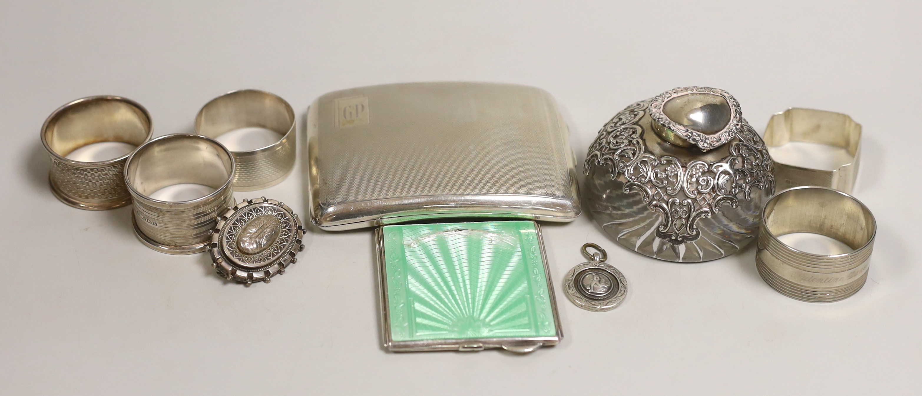 A quantity of mixed silver ware including a cigarette case and enamelled compact (a.f.), a mounted glass inkwell, five napkin rings, (one plated), a brooch and a Fattorini & Sons football pendant.